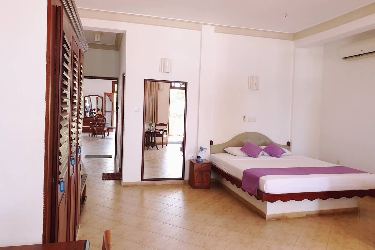 Un dormitorio con una cama, un ventilador de techo y una puerta que da a un comedor.