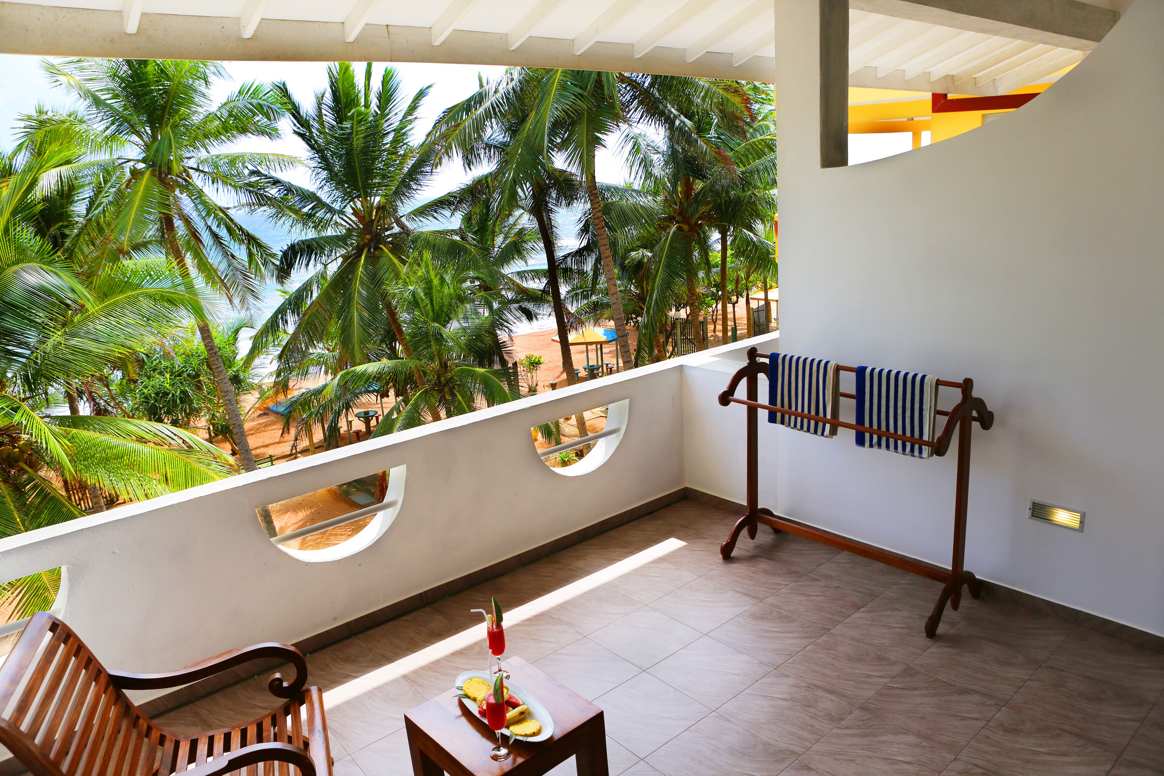 A balcony with a wooden bench, a small table with a drink, and a towel rack.