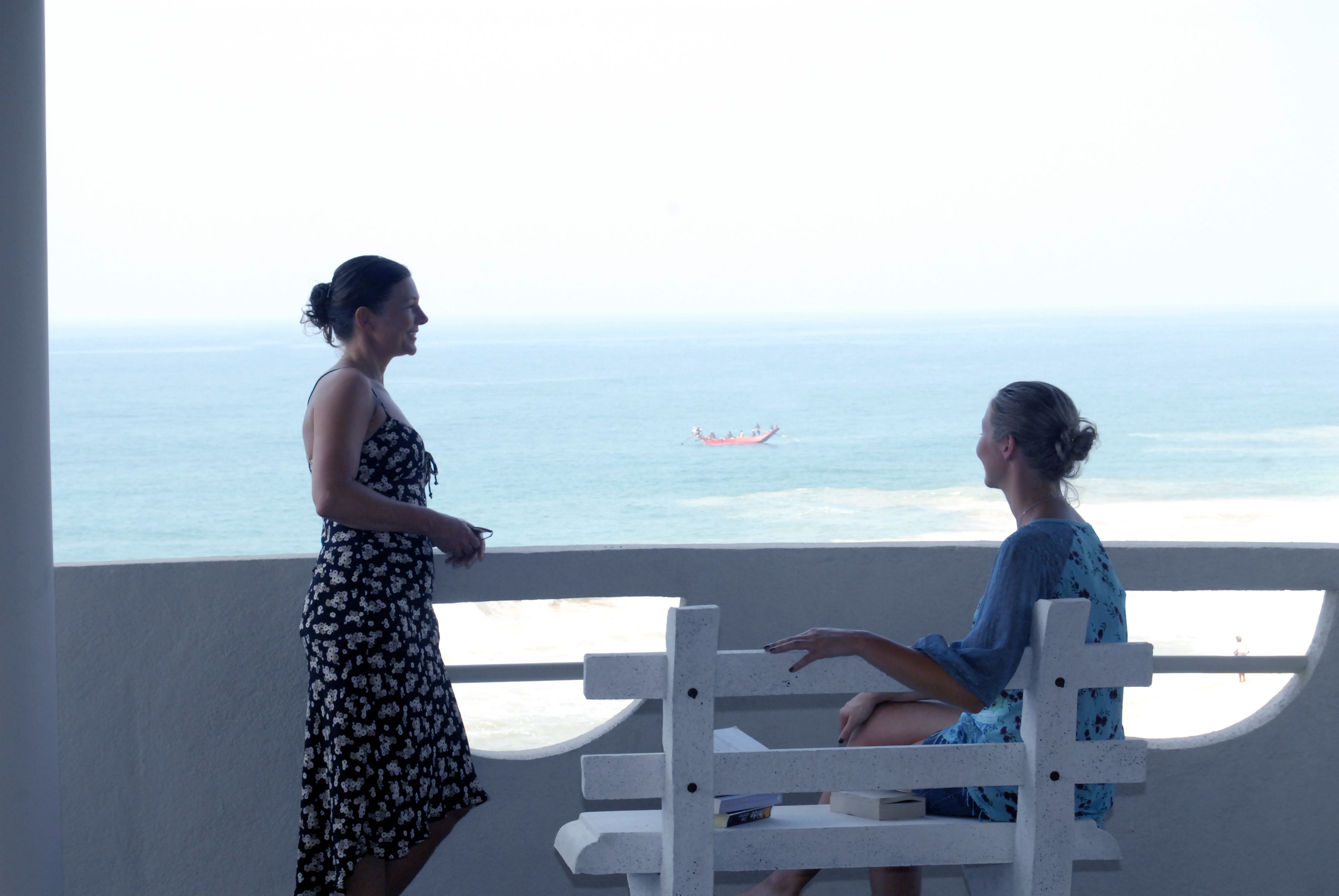 Deux femmes sont assises sur un banc blanc, près d’une fenêtre donnant sur l’océan.