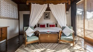 A bedroom with a canopy bed, wooden furniture, and a view through large windows.