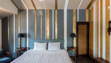 A hotel room with a large bed, two bedside tables with lamps, a blue armchair, and a door.