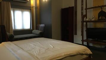 Une chambre d’hôtel avec un lit, une chaise, un téléviseur posé sur un meuble en bois, un appareil de climatisation et une fenêtre avec des rideaux.