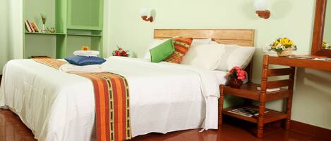 A neatly arranged bedroom with a large bed, a wooden chair, a small table with a vase, and a green shelving unit.