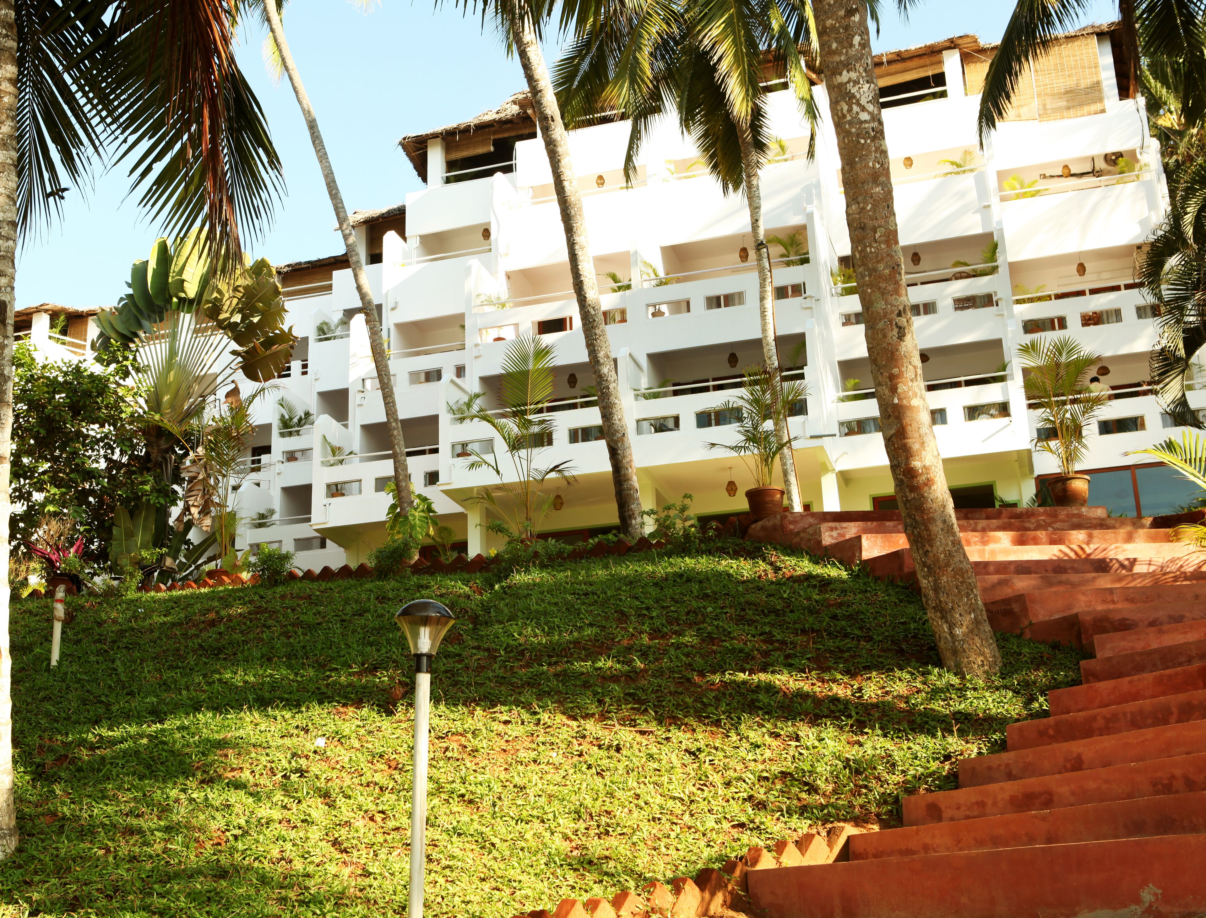 A multi-story building with balconies, surrounded by palm trees and greenery.