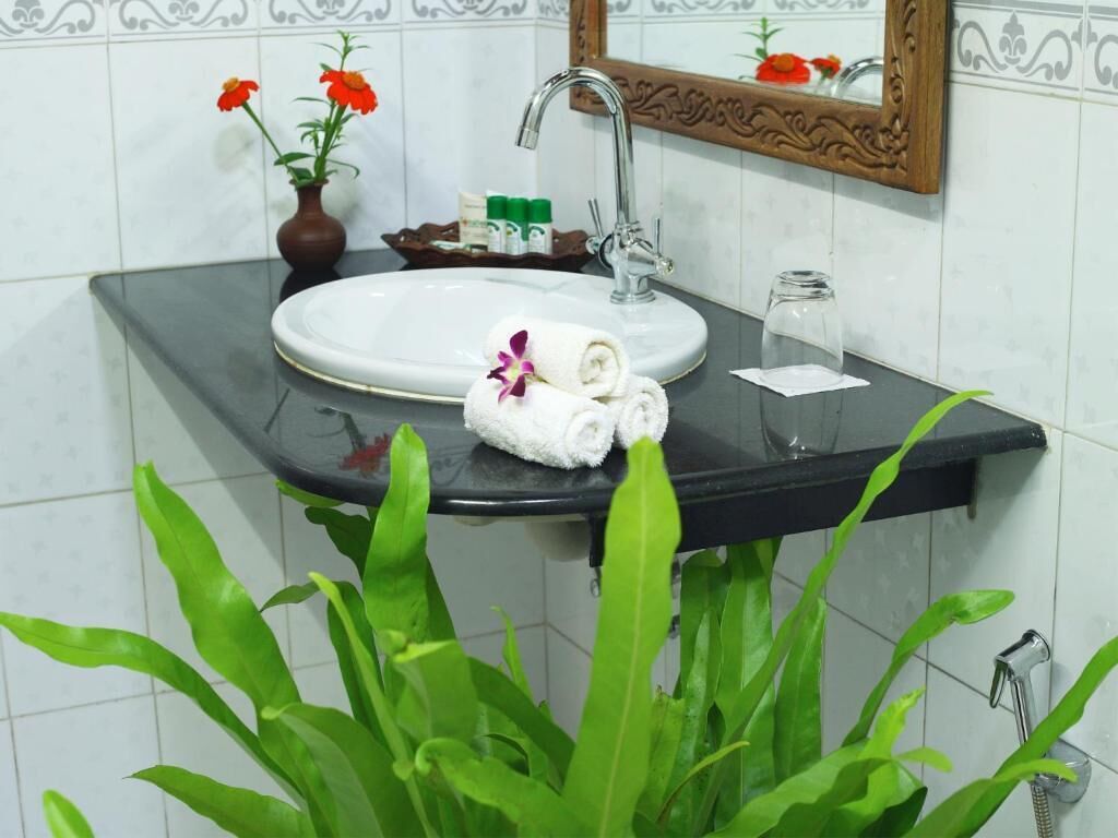 Un baño con un lavamanos blanco, un espejo y plantas verdes.