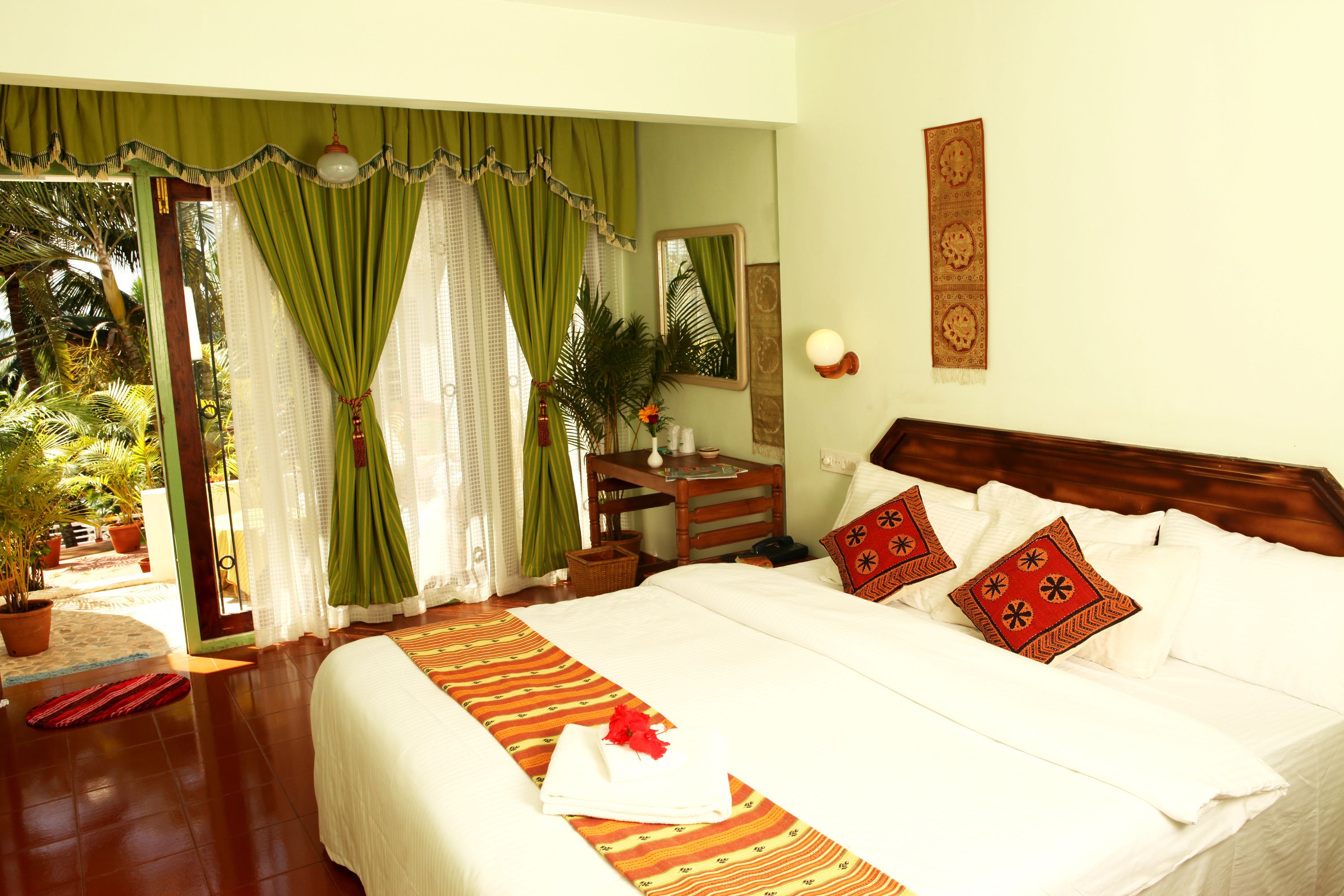 A hotel room with a bed, a desk, a chair, a mirror, and a window with curtains.