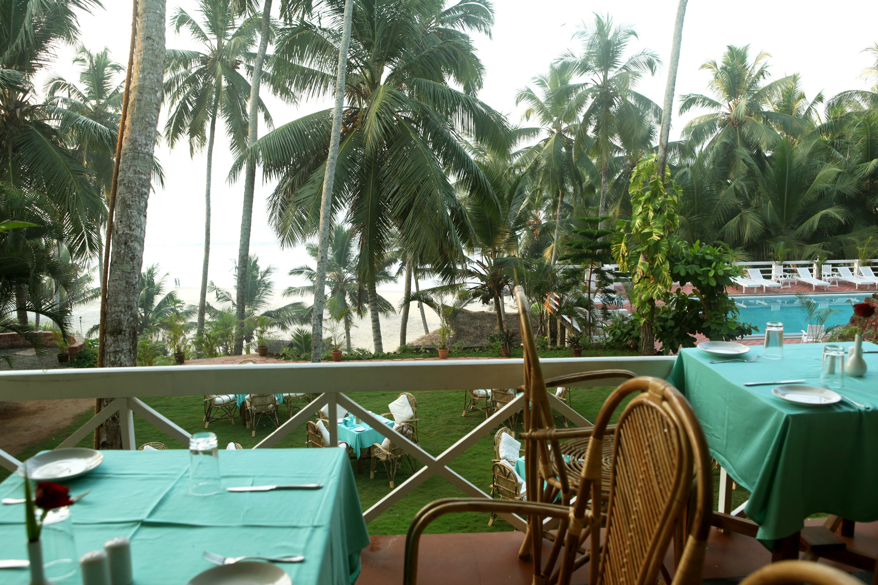 An outdoor dining area with tables set for two, overlooking a pool and palm trees.