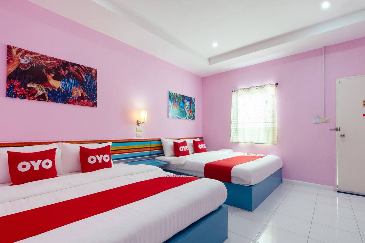 Habitación de hotel con dos camas, cada una con ropa y almohadas rojas y blancas, paredes rosadas y cuadros en las paredes.