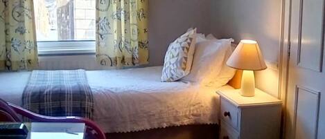 A neatly made bed with a plaid blanket, a bedside lamp, and a window with curtains.