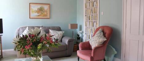 A living room with a grey sofa, a red armchair, a bookshelf, and a framed picture on the wall.