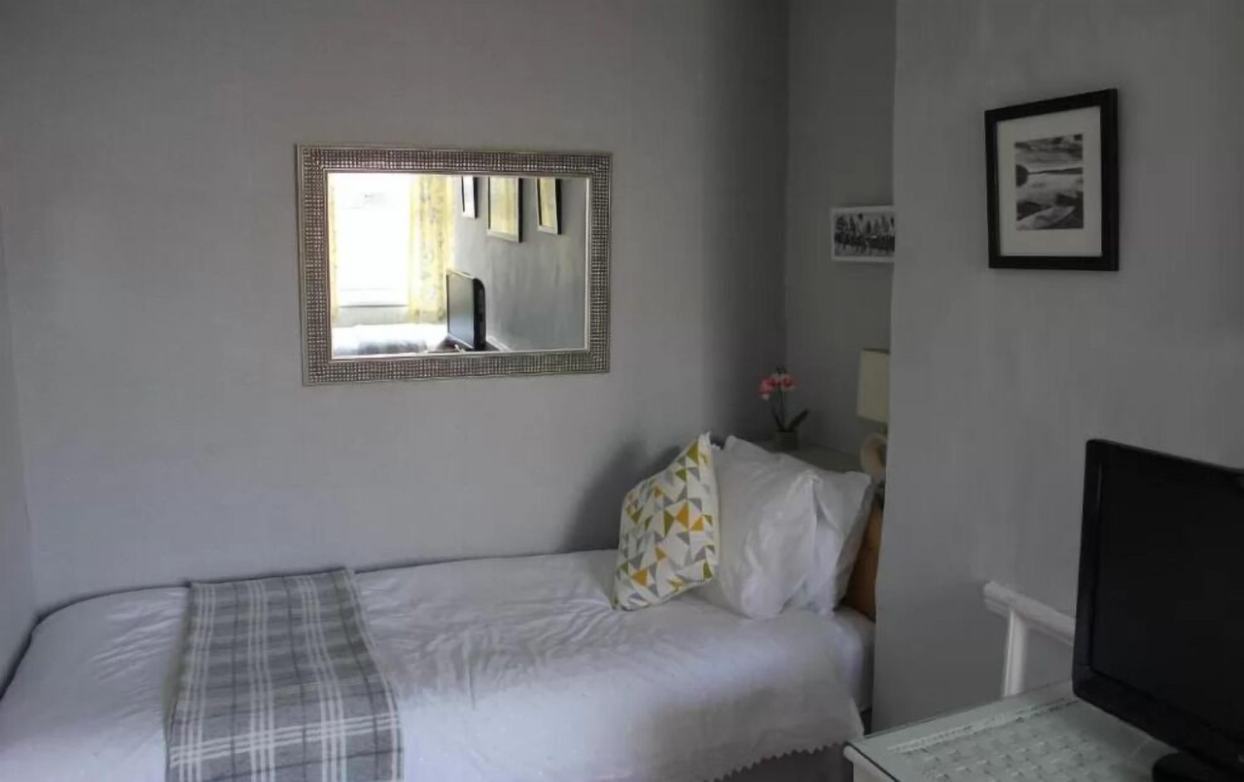 A bedroom with a bed, a TV, a mirror, and a framed picture on the wall.