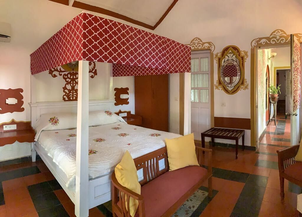 A four-poster bed with a red canopy, a wooden bench, and a mirror on the wall.