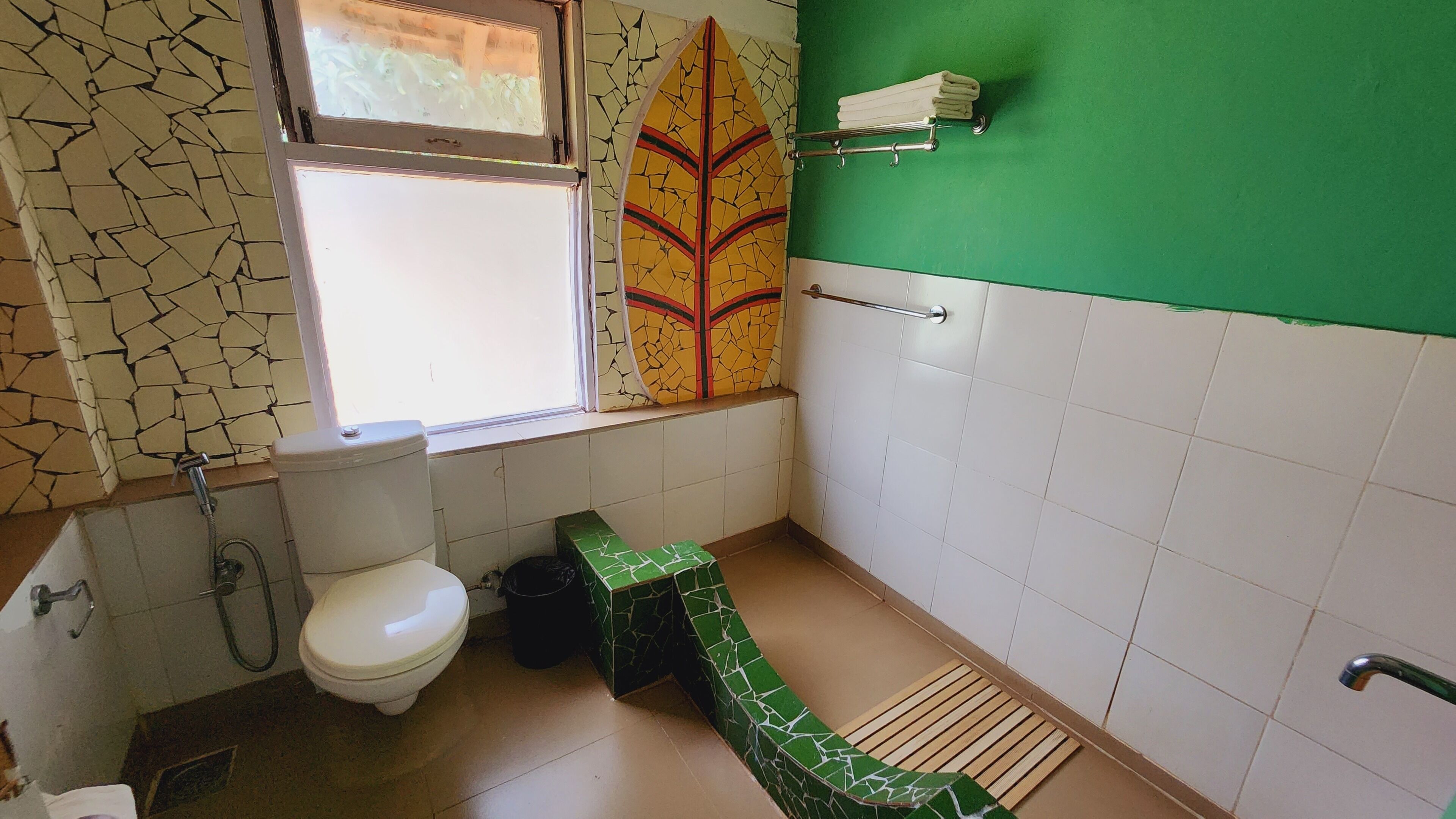 A bathroom with a toilet, a green sink, a window, and a towel rack.