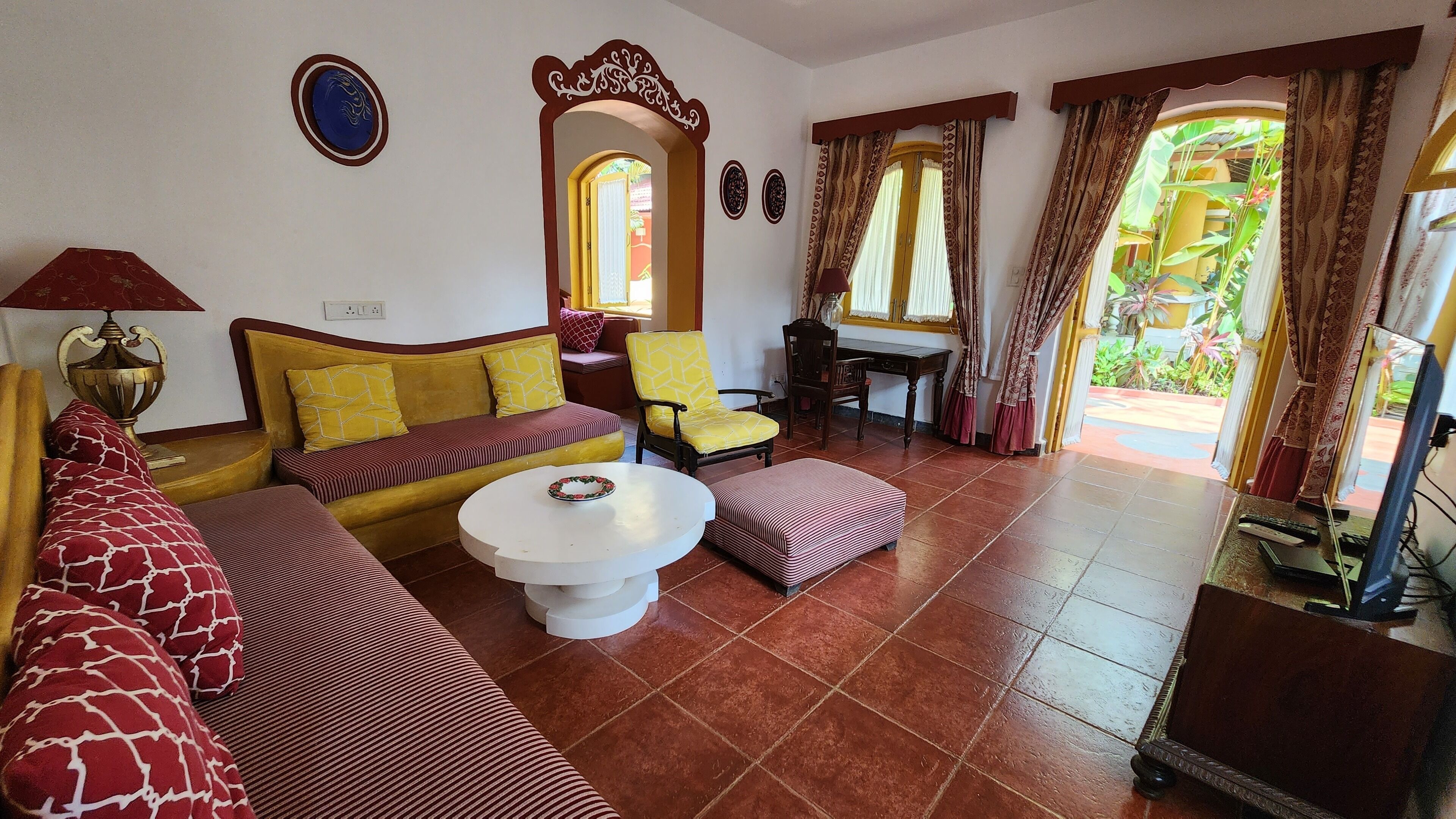 Una sala de estar con sofá, sillón, reposapiés, una mesa de centro redonda y un televisor.
