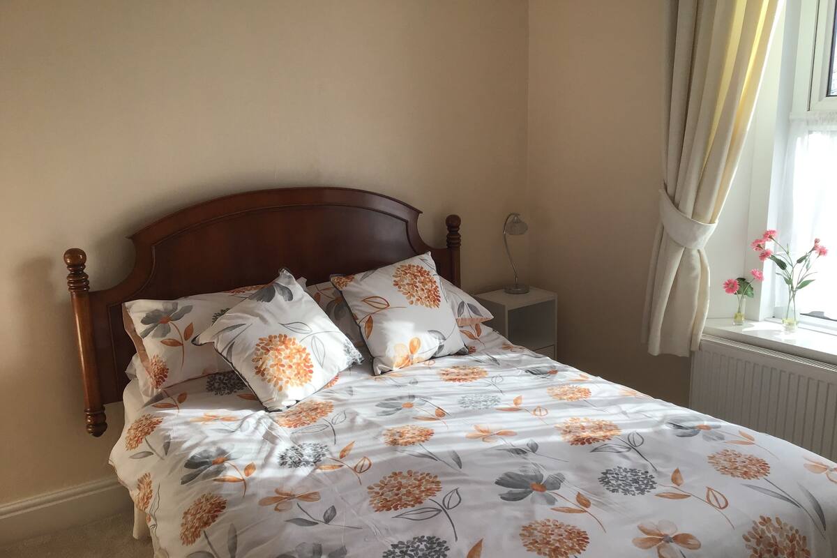 A bed with a floral-patterned bedspread, a wooden headboard, and two bedside tables with lamps.