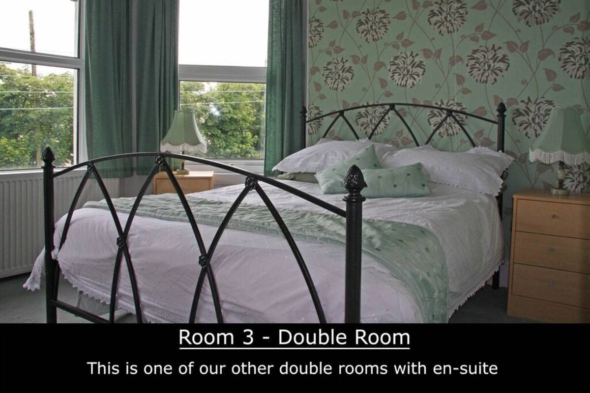 A double room with an en-suite bathroom, a bed with a metal frame, a nightstand, a dresser, and a window with curtains.