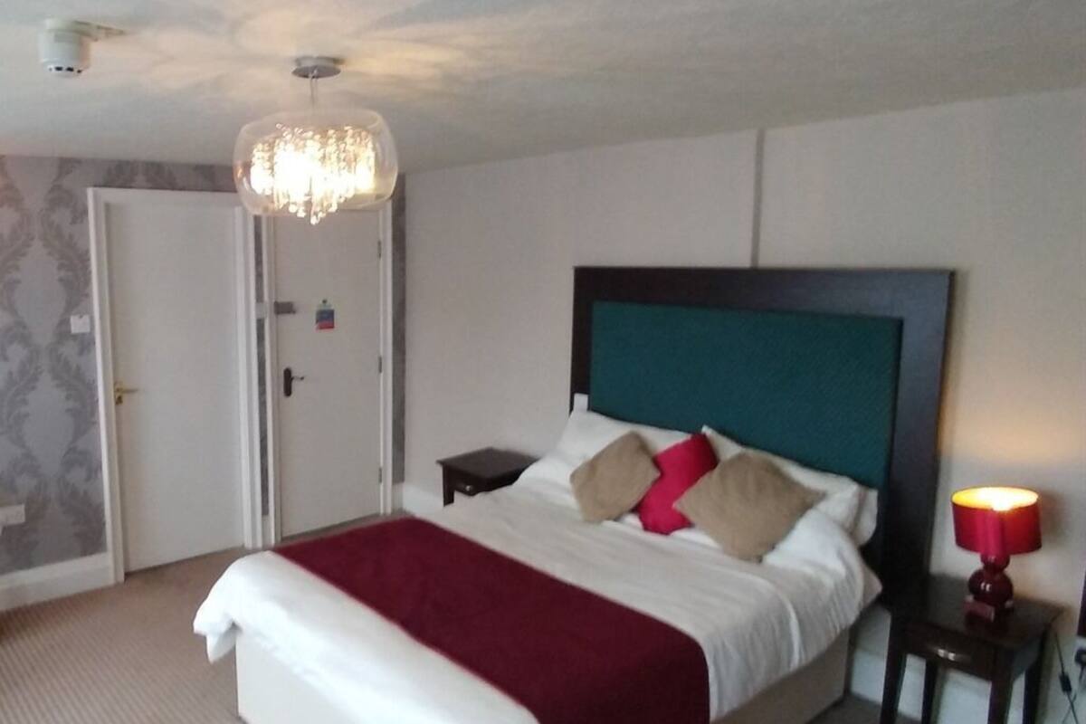 A hotel room with a large bed, a nightstand, a lamp, and a door.