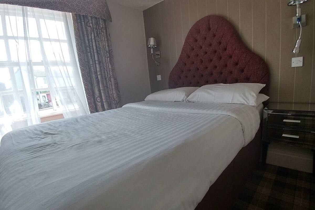 A neatly made bed with a tufted headboard, a bedside lamp, and a checkered floor.