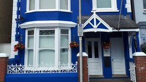 A two-story house with a bay window and a front door, painted in blue and white. - Glenholme Apartments (Tenby)