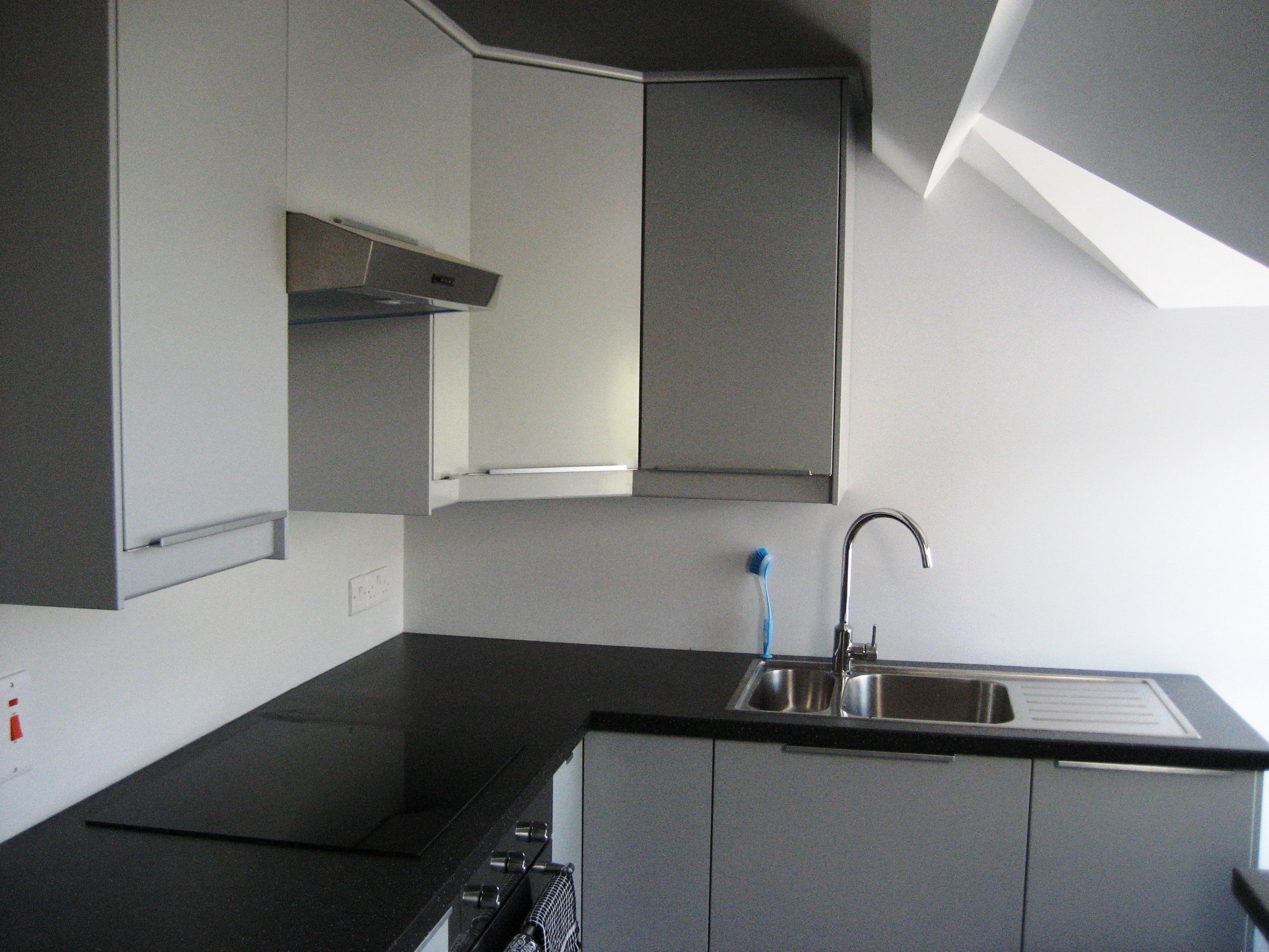 A kitchen with a black countertop, stainless steel sink, and grey cabinets.