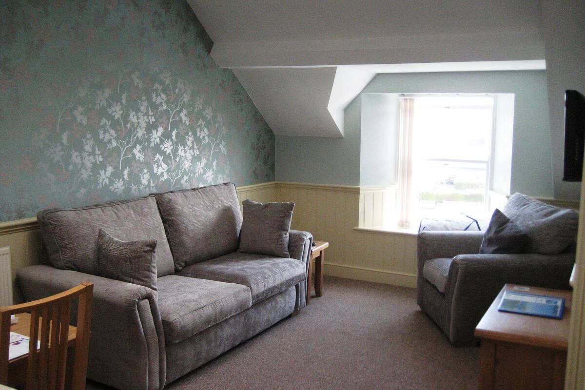 A cozy living room with a grey sofa, a wooden chair, and a small table.