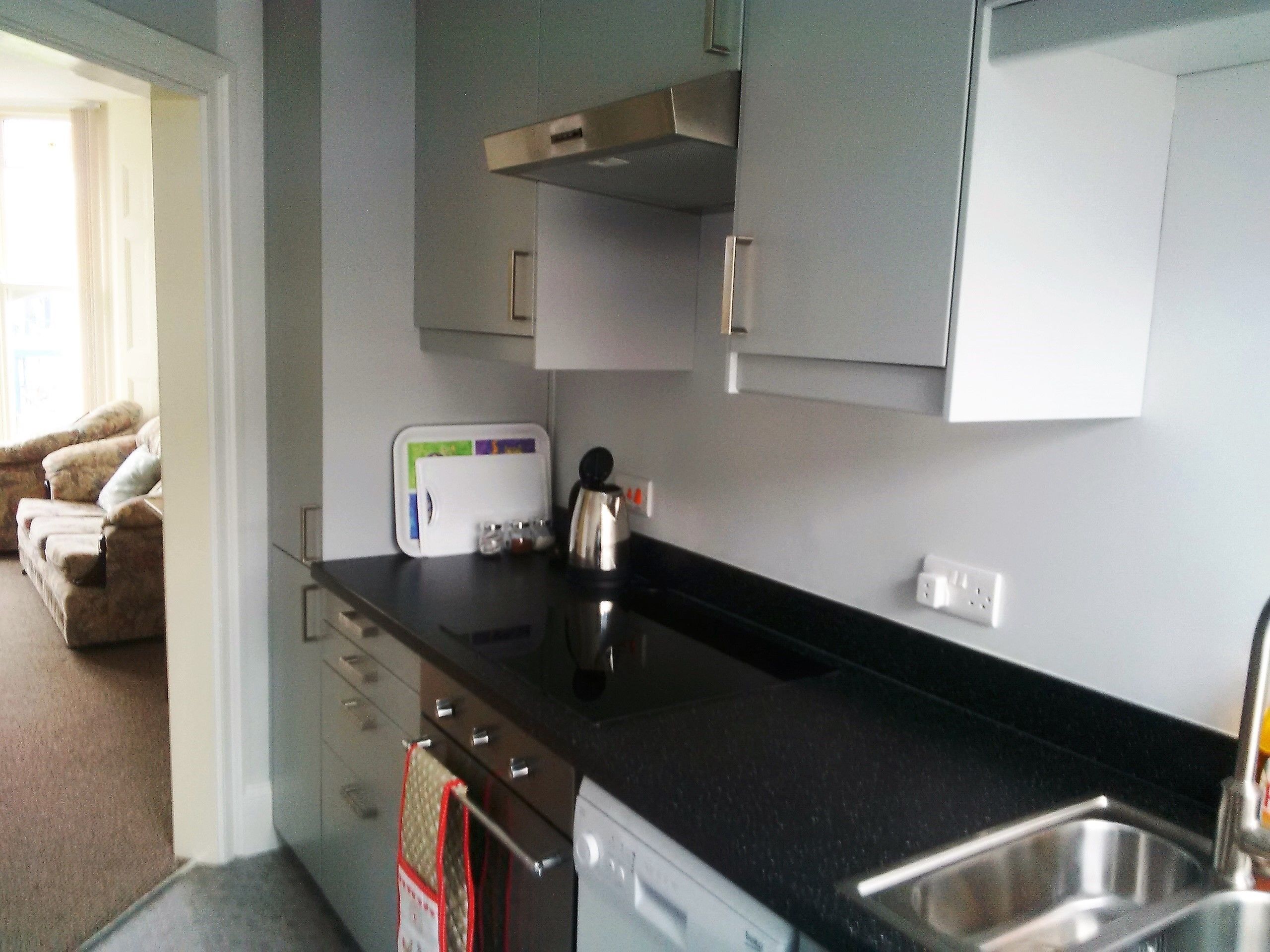 A compact kitchen with a black countertop, stainless steel sink, and a coffee maker.