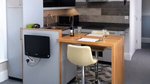 A compact kitchen with a built-in microwave, a sink, and a small dining area with a bar stool. - Glenholme Apartments (Tenby)