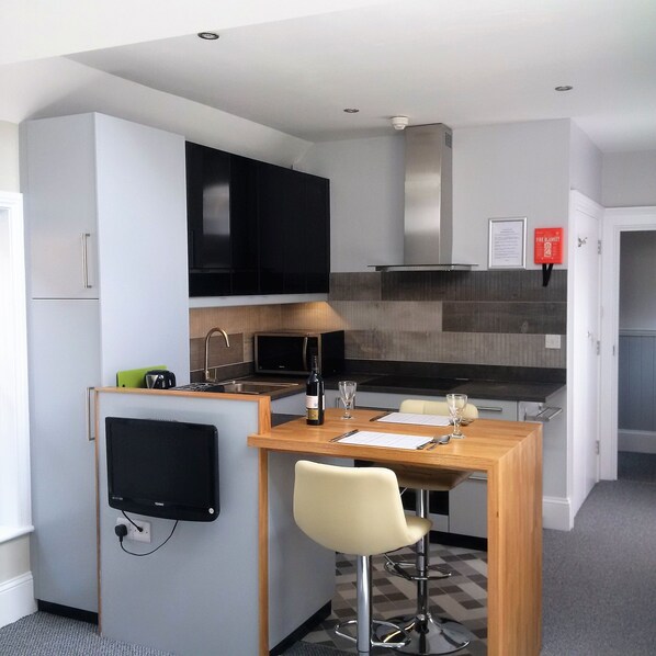 A compact kitchen with a built-in microwave, a sink, and a small dining area with a bar stool. - Glenholme Apartments (Tenby)