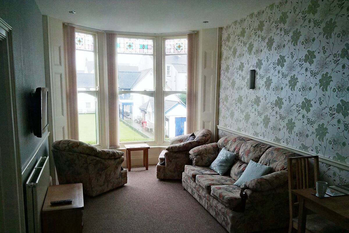 A living room with a sofa, armchairs, a small table, and a television.