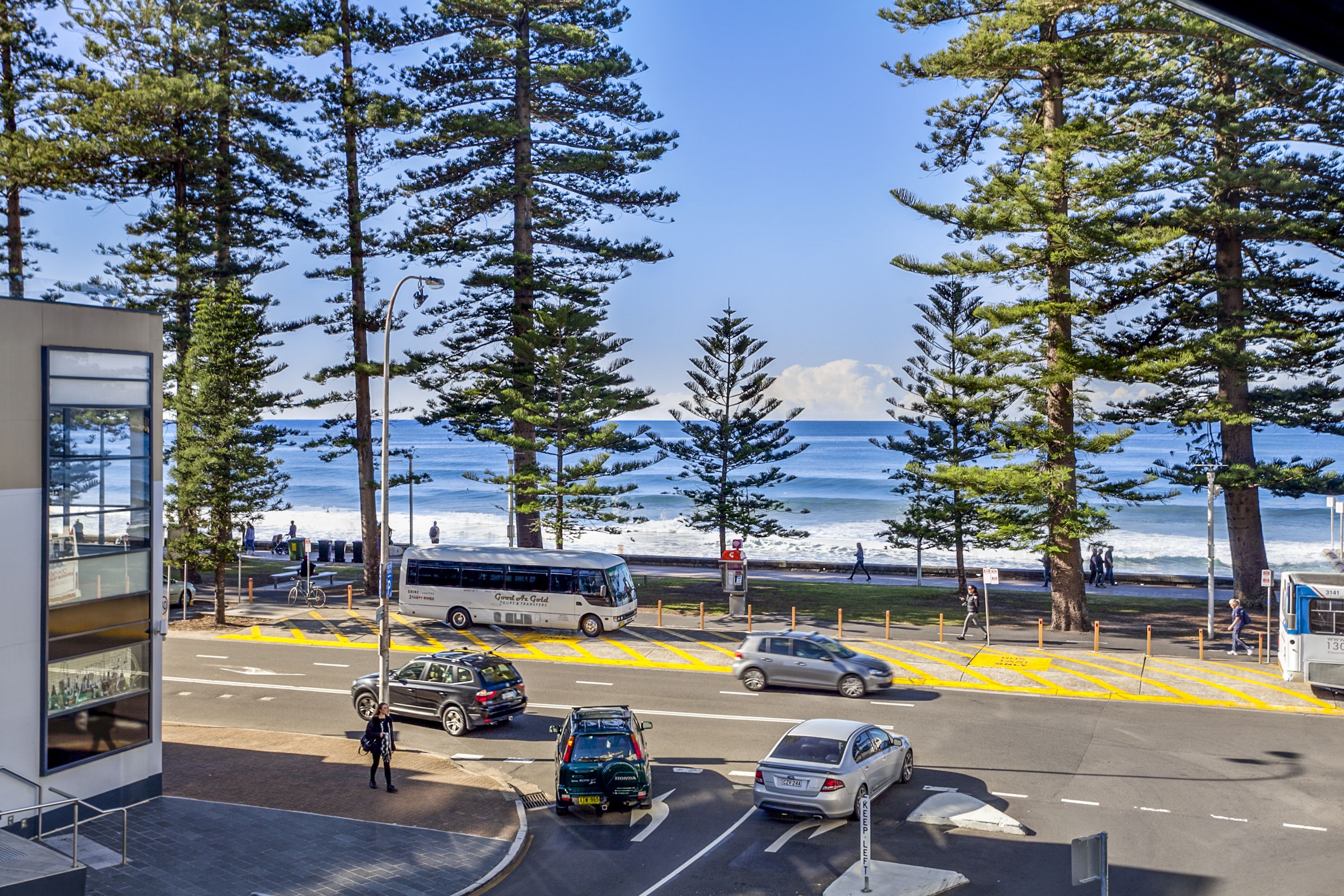 A coastal street with a bus, cars, and pedestrians.