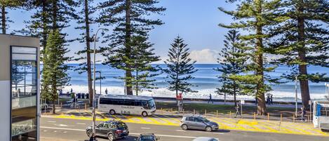 A coastal street with a bus, cars, and pedestrians.
