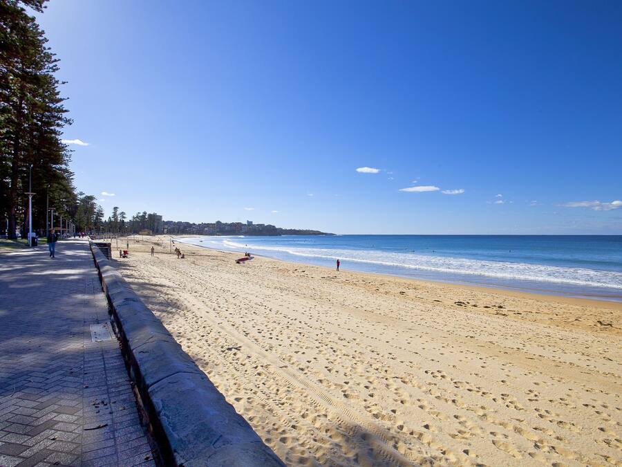 A wide sandy beach with a paved walkway on the left, leading to the water.
