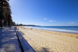 A wide sandy beach with a paved walkway on the left, leading to the water. - Manly Paradise Motel & Apartments (Manly)
