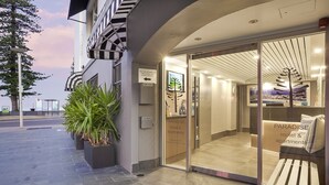 L'ingresso moderno di un hotel con una porta in vetro, un cartello per Paradise Motel & Apartments e una panchina all'esterno.