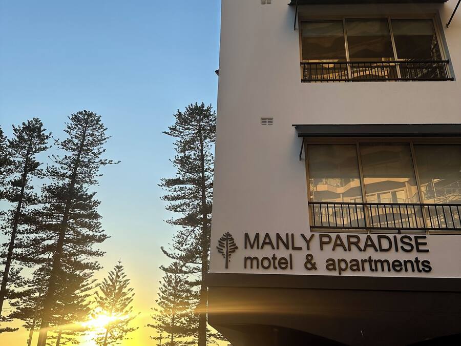 A building with a sign for "Manly Paradise motel & apartments" featuring a modern design with multiple windows and balconies.