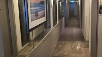 A hotel corridor with a long hallway, mirrored walls, and a framed picture of a beach scene.