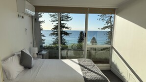 Una camera da letto con un letto, un comodino, una lampada e vista mare attraverso ampie finestre.