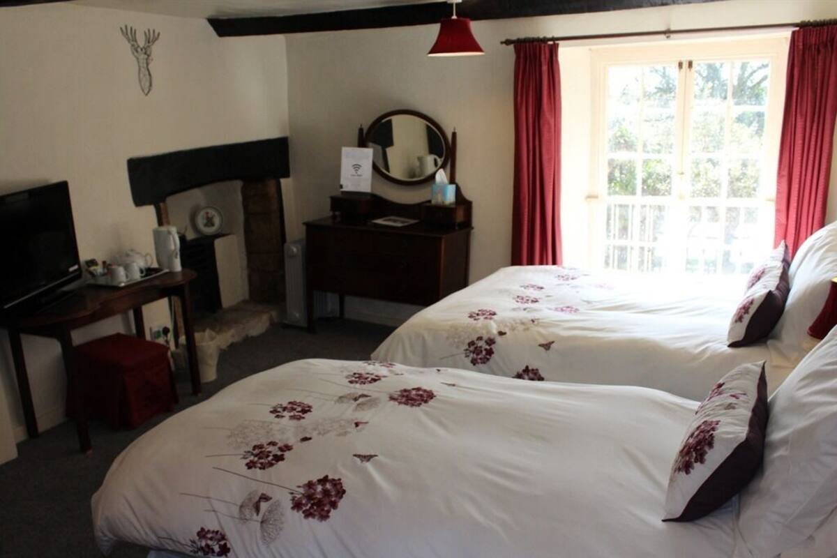 Ein Hotelzimmer mit zwei Betten, einem Schreibtisch, einem Fernseher und einem fensterbepflanzten Fenster.