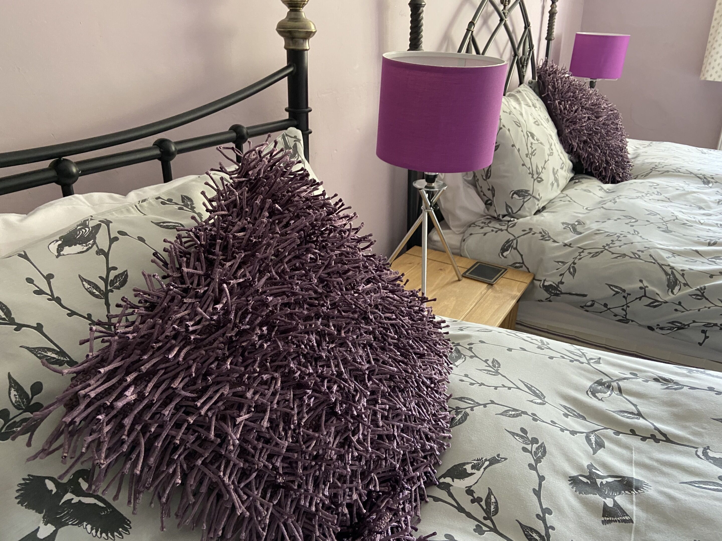 A bed with floral bedding, a purple textured pillow, and a bedside lamp.
