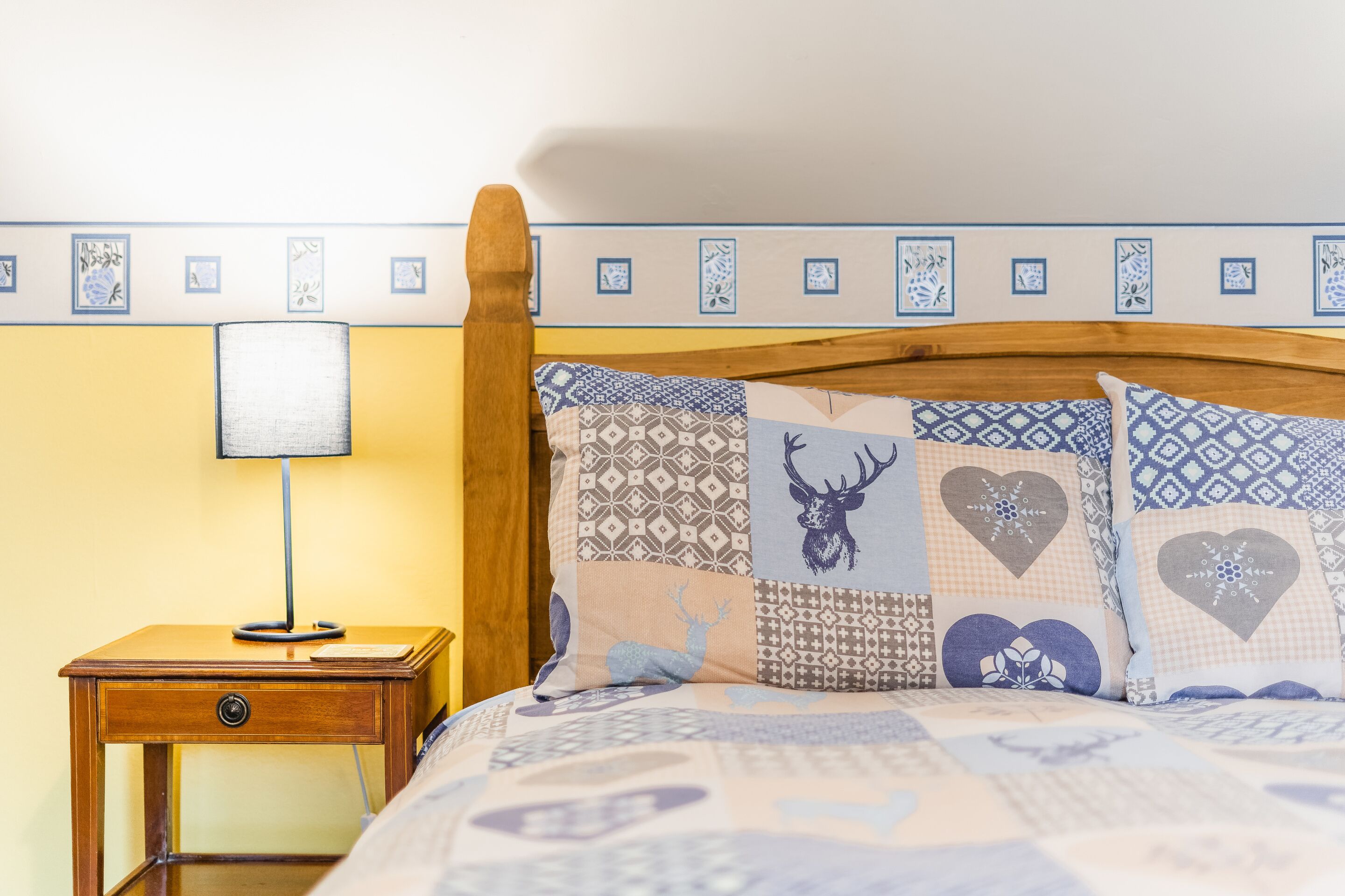 Una cama con almohadones estampados, un cabecero de madera y una mesita de noche con lámpara.