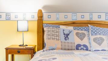 Una cama con almohadones estampados, un cabecero de madera y una mesita de noche con lámpara.