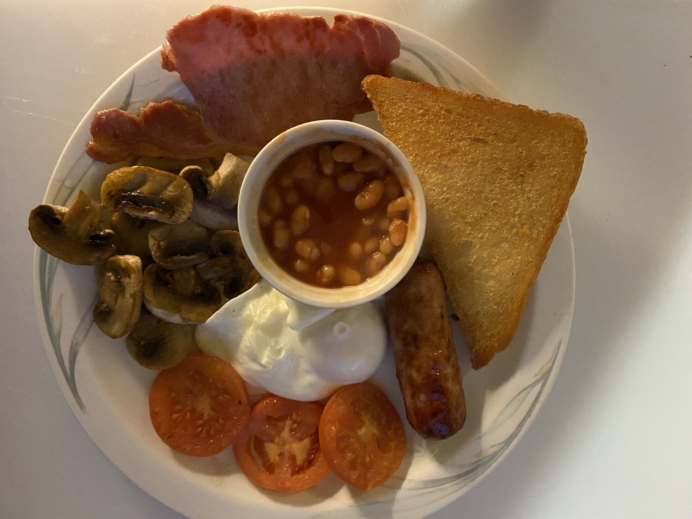 A plate with bacon, mushrooms, beans, toast, sausage, and tomatoes.