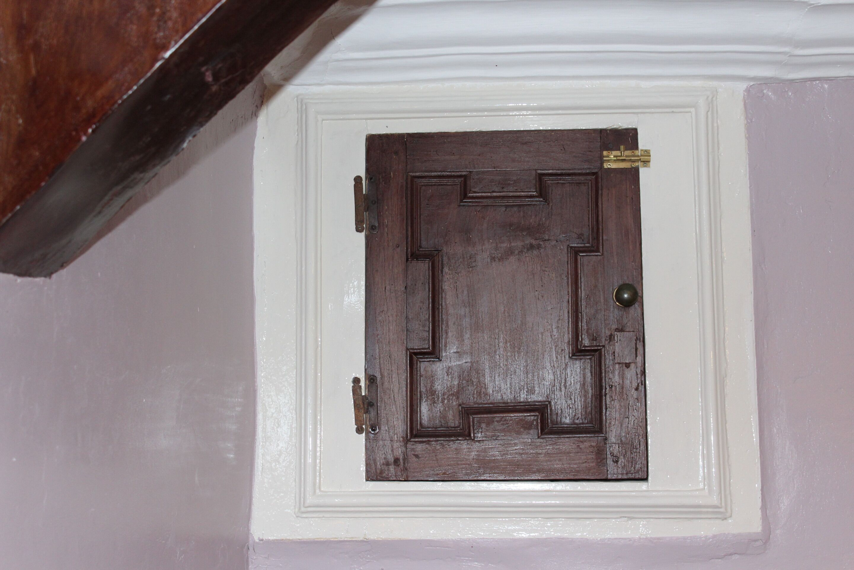 A wooden door with a brass handle and a brass doorknob, set in a white wall with a decorative molding.