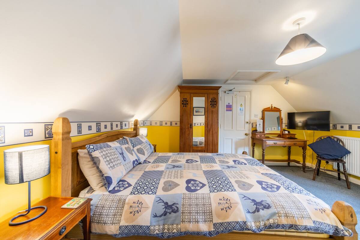 Ein Schlafzimmer mit Bett, Nachttisch, Lampe, Schreibtisch, Stuhl und einem Fernseher.