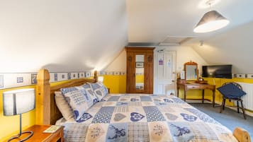 Un dormitorio con cama, mesita de noche, lámpara, escritorio, silla y televisor.