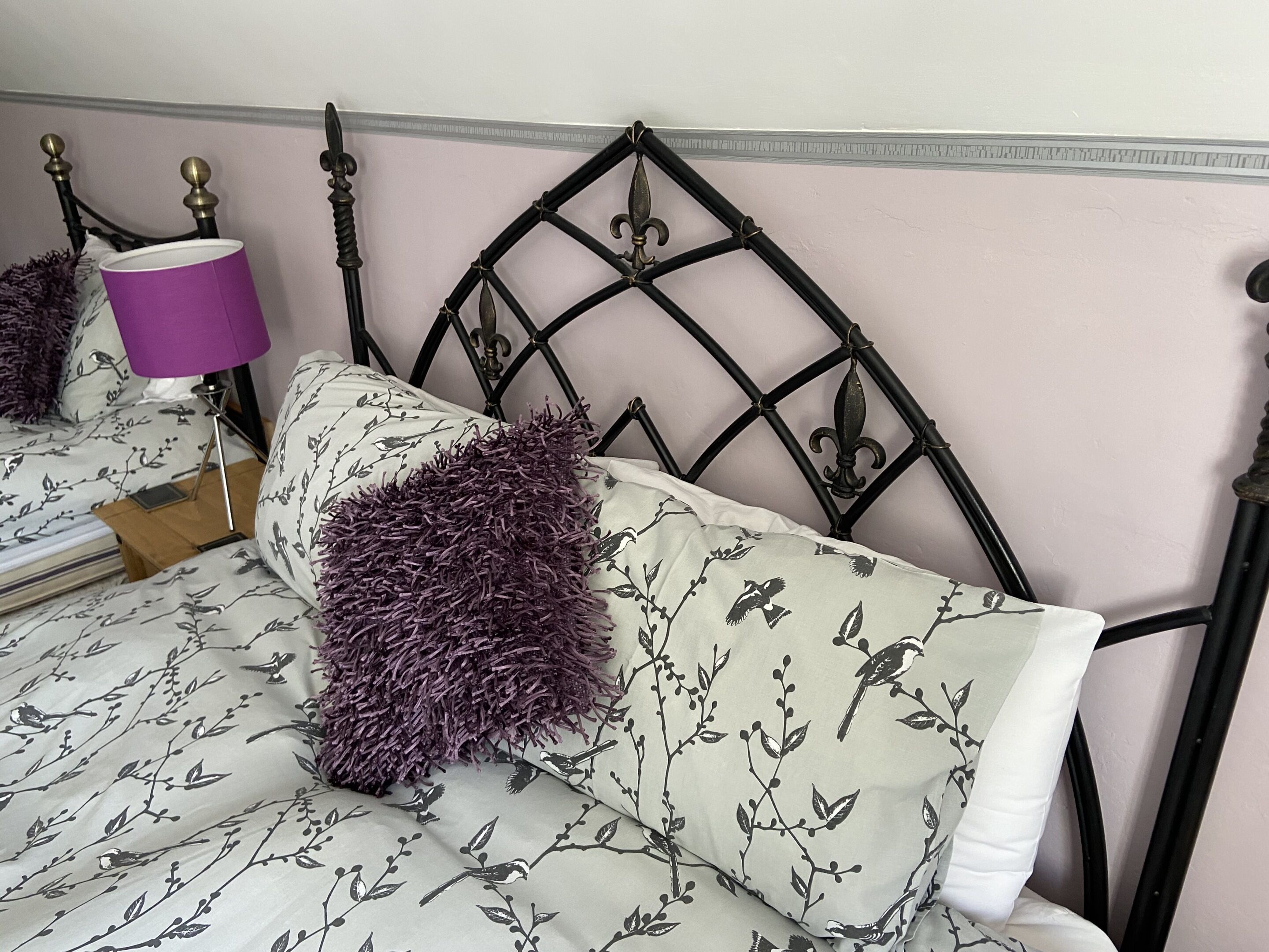 A bed with a headboard, a purple lamp, and floral-patterned bedding.