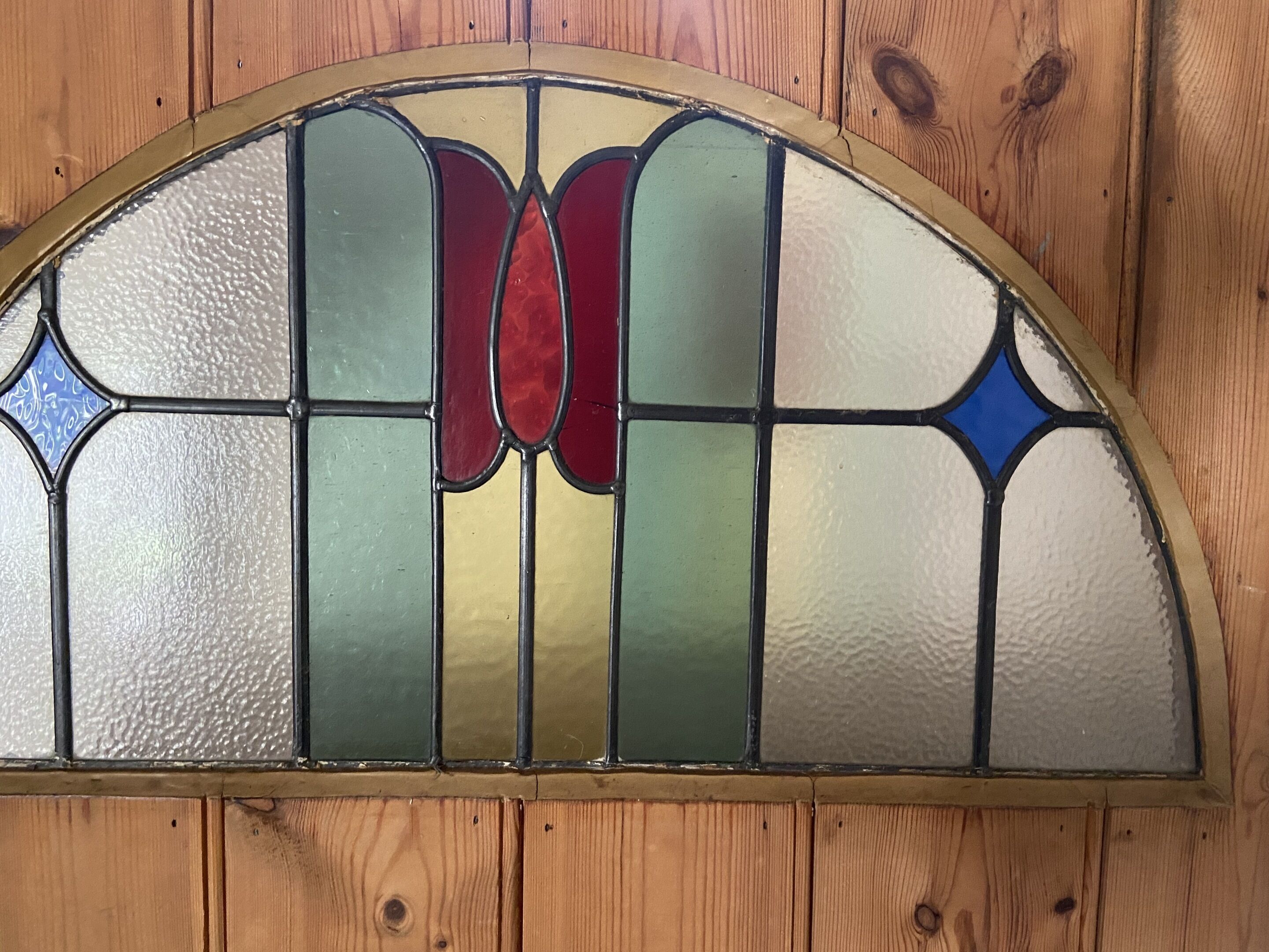 Una ventana de vitral con parte superior semicircular y una cuadrícula de vidrios de colores.