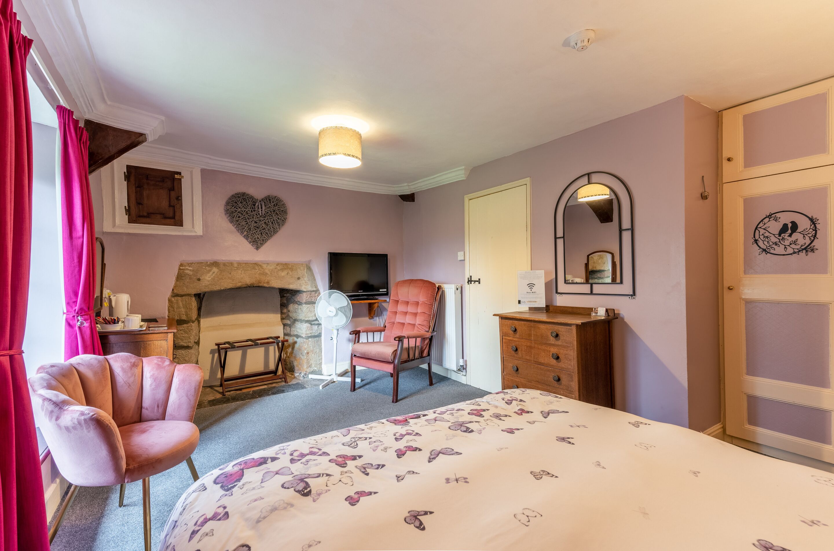 A bedroom with a bed, a chair, a dresser, a mirror, a fireplace, and a door.
