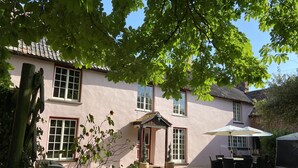 A two-story house with a pink facade, a tiled roof, and a small porch area with a potted plant. - Yallands Farmhouse (Taunton)