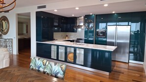 A modern kitchen with dark cabinets, a stainless steel refrigerator, and a built-in island with a sink. - Honeysuckle Executive Apartments (Newcastle)